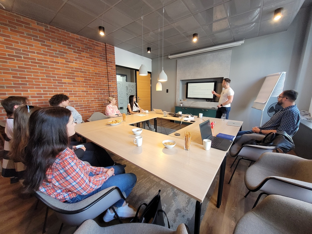 wizja lokalna studentów EkSocu w Animalhotels.com - grupa studentów siedzi wokół syołu i słucha prezentacji Łukasza Klaba