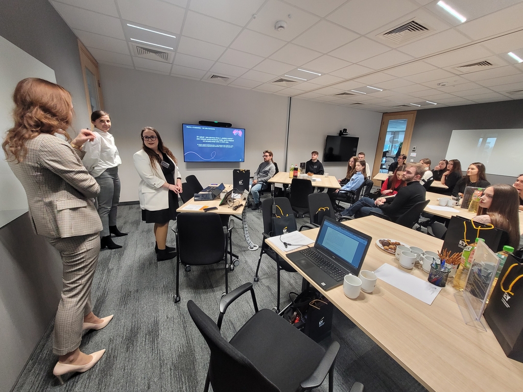 Trzy pracownice EY opowiadają studentom siedzącym przy biurkach w siedzibie EY o funkcjonowaniu EY. Wizyta realizowana w ramach projektu Mapa Biznesowa Łodzi - Wizja Lokalna - EY 21.02.2024