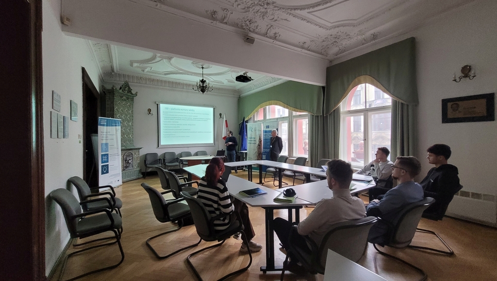 wizja lokalna w FRP 6.03.2024 - pracownicy FRP prowadzą prelekcję dla grupy studentów EkSocu siedzących przy stole