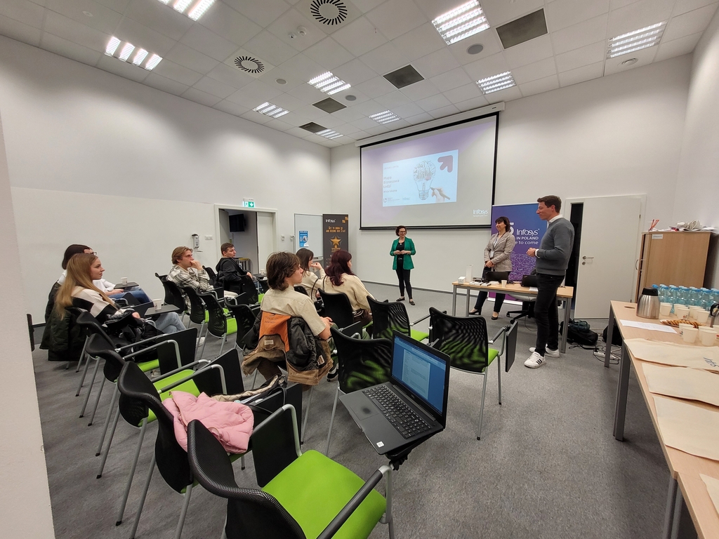 Mapa Biznesowa Łodzi - Wizja Lokalna - Infosys 17.04.2024 - siedmioro studentów siedzi na krzesłach i przygląda się prezentacji prowadzonej na stojąco przez troje pracowników firmy