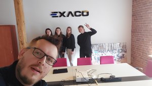 Mapa Biznesowa Łodzi - Wizja Lokalna - Exaco 17.04.2023 - na pierwszym planie pracownik firmy a wtle grupa studentów pod logotypem firmy