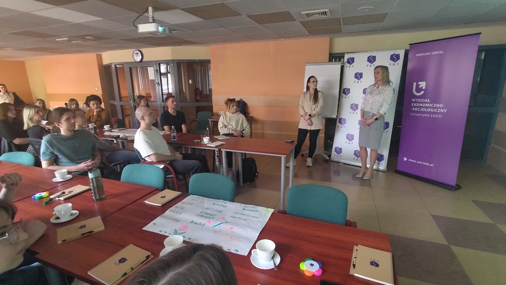 szkolenie pt. Autoprezentacja i radzenie sobie ze stresem - Polska Grupa Farmaceutyczna - 14.04.2025 - studenci siedzący przy stołach słuchają co mówi Prowadząca szkolenie i druga osoba z PGF, widok ogólny na salę