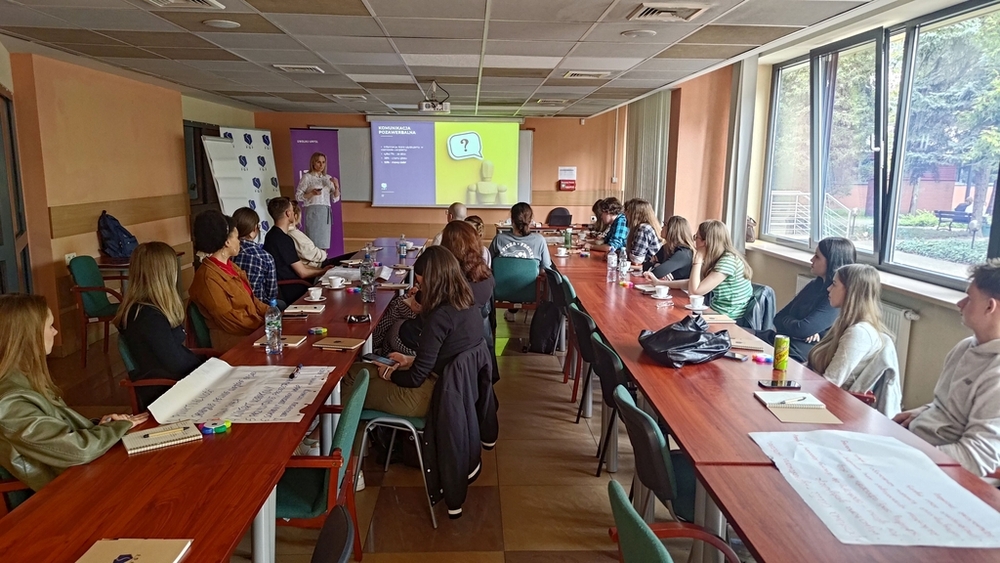 szkolenie pt. Autoprezentacja i radzenie sobie ze stresem - Polska Grupa Farmaceutyczna - 14.04.2025 - studenci siedzący przy stołach słuchają co mówi Prowadząca szkolenie, widok ogólny na salę